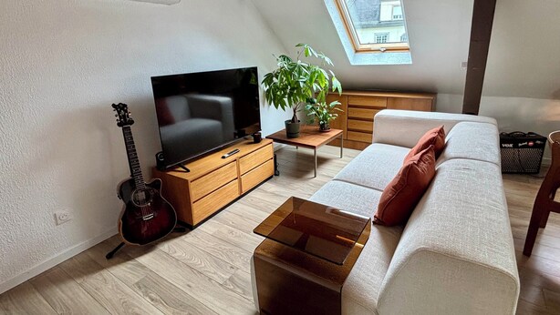 Una sala de estar con televisión, una guitarra, un sofá, una mesa de centro y una planta.