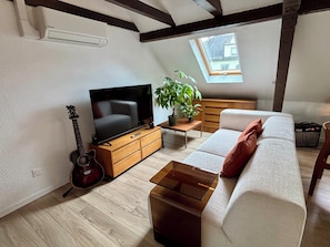 Ein Wohnzimmer mit Fernseher, Gitarre, Sofa, Couchtisch und einer Pflanze.