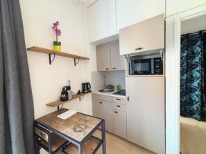 Eine kleine Küche mit Mikrowelle, Kaffeemaschine und einem Tisch mit einer Pflanze.