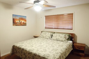 A bedroom with a bed, a ceiling fan, a window with blinds, a nightstand, and a wall-mounted painting. - Cozy 2-bedroom condo in peaceful Parowan (Parowan)