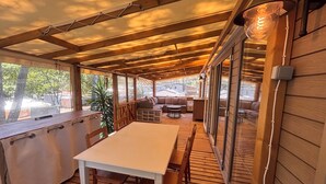 A covered outdoor deck with a wooden table and chairs, a sofa, and a dining area. - Chalet in a 5-star resort with swimming pool (Puget-sur-Argens)