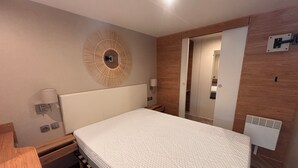 A bedroom with a bed, bedside tables, a wall-mounted lamp, a mirror, and a wooden panel wall. - Chalet in a 5-star resort with swimming pool (Puget-sur-Argens)