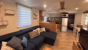 A modern living room with a sectional sofa, a kitchen in the background, and a dining area. - Chalet in a 5-star resort with swimming pool (Puget-sur-Argens)