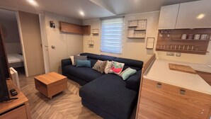 A compact living space with a sofa, coffee table, kitchenette, and a window with blinds. - Chalet in a 5-star resort with swimming pool (Puget-sur-Argens)