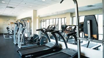 A gym with multiple treadmills and exercise machines, large windows, and a tiled ceiling.