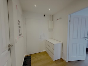 Ein Zimmer mit einer weißen Tür, einem kleinen weißen Schrank, einem Holzboden und einer wandmontierten Leuchte.
