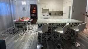 A modern kitchen with a central island, bar stools, a dining table with chairs, and a patterned floor. - Spacious newly renovated two bedroom apartment (Sault Ste. Marie)