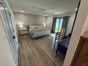 Ein Schlafzimmer mit Bett, Nachttischen, Schreibtisch, Stuhl, Deckenventilator und Blick ins Freie.