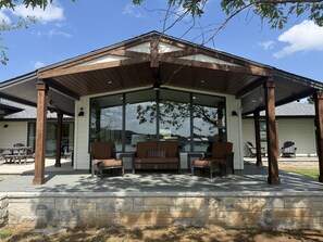 Eine überdachte Terrasse mit Steinmauern, großen Fenstern und Gartenmöbeln.