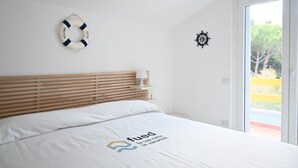 Ein Schlafzimmer mit einem hölzernen Kopfteil, einem Bett mit weißer Bettwäsche, einer Rettungsboje als Dekoration, einem Schiffsrad und Blick auf Grünfläche draußen.