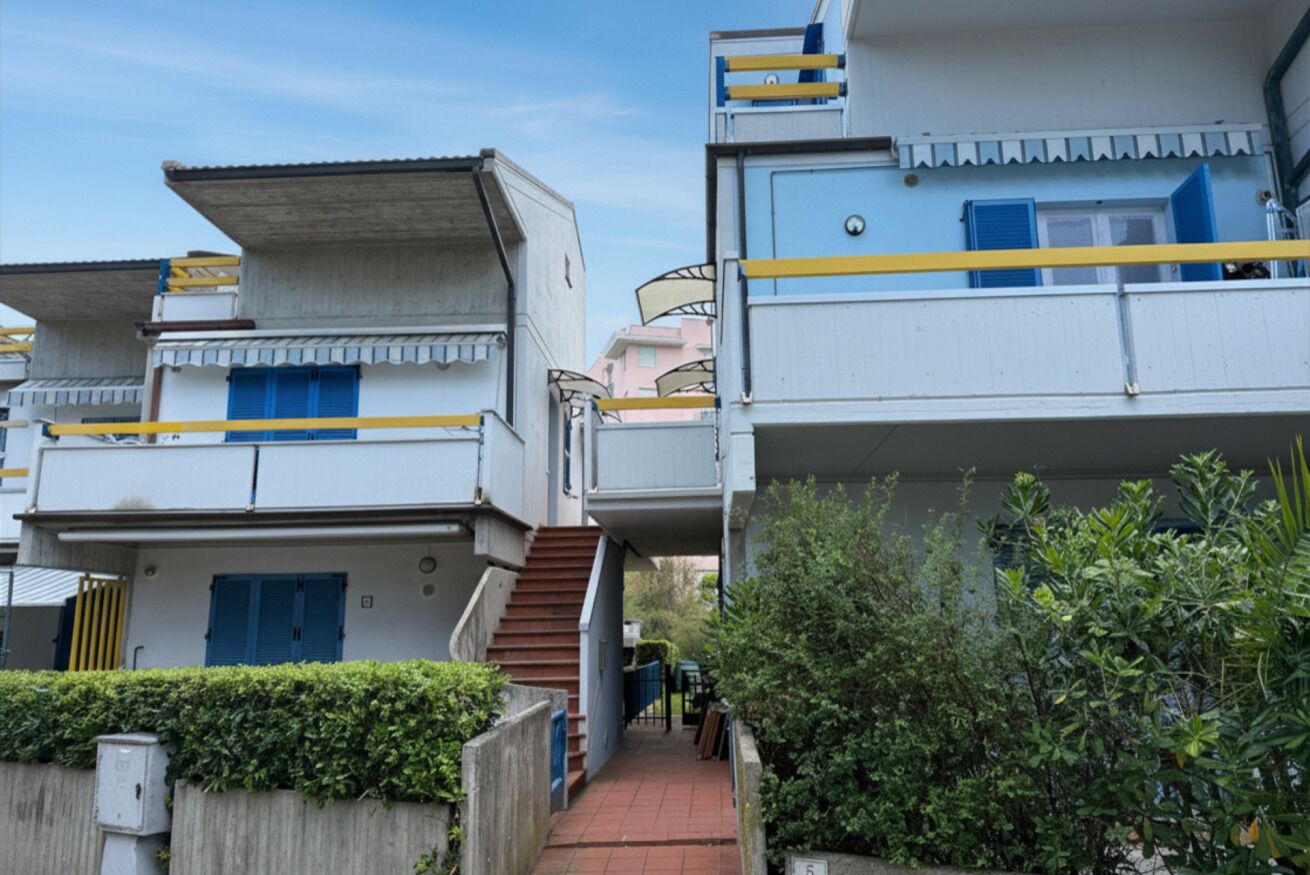 Un immeuble résidentiel avec un escalier menant à un balcon, le tout entouré de verdure.