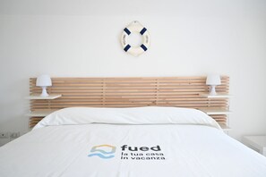 Ein Bett mit weißer Bettdecke und einem Logo, ein Holz-Kopfteil, zwei Nachttischlampen und ein Rettungsring an der Wand.