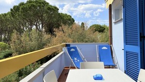 Ein Balkon mit Tisch und Stühlen, einer blauen Liege und einer türartigen blauen Abschirmung.