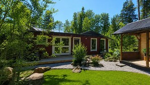 Uma cabana com varanda, um alpendre coberto e um jardim com pedras e plantas.