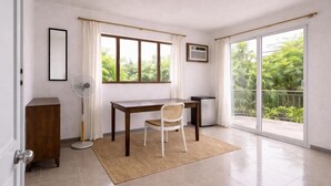 A room with a desk, chair, fan, and a view of greenery through a sliding door. - ISLO APT (General Luna)
