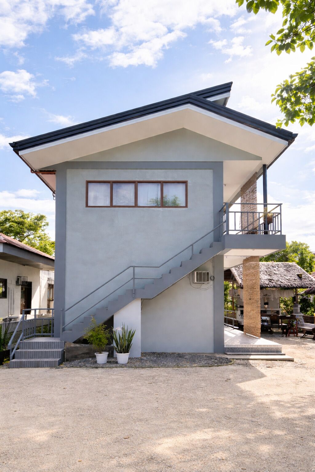 A modern two-story building with a staircase, a balcony, and a small garden area.