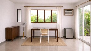 A room with a wooden desk, a white chair, a standing fan, a small cabinet, and a window with curtains. - ISLO APT (General Luna)