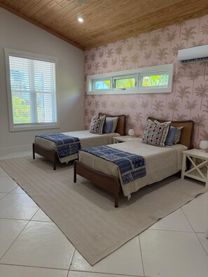 Ein Schlafzimmer mit zwei Betten, einem großen Fenster, einem Deckenventilator und einer Wand-Klimaanlage.