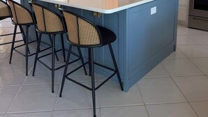 Una cuina amb una illa gran, tamborets d'esbarjo, un frigorífic i una placa de cocció.