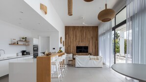 Une cuisine moderne dotée d’un îlot central, de tabourets de bar, d’un coin repas avec une table ronde et d’un téléviseur fixé à un mur en bois.