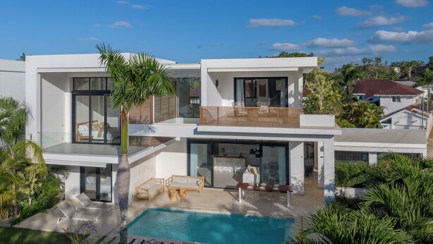 Une maison moderne à deux étages, dotée d’une piscine, d’un espace de détente extérieur et d’une végétation luxuriante.