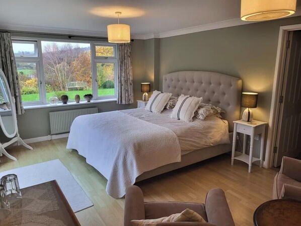 A bedroom with a large bed, two bedside tables, a chair, and a view of the outdoors. - 2bed-sleeps4-petsok-courtyard & Garden (Totnes)