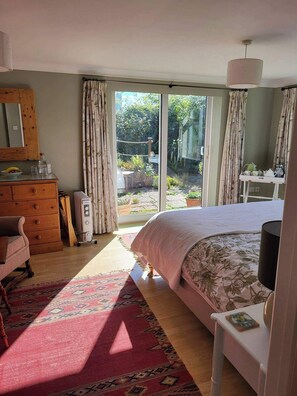 A bedroom with a bed, dresser, and a view of the garden through a sliding door. - 2bed-sleeps4-petsok-courtyard & Garden (Totnes)