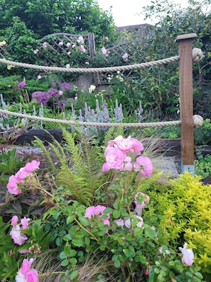 A garden with a wooden trellis, various flowering plants, and a rope structure. - 2bed-sleeps4-petsok-courtyard & Garden (Totnes)