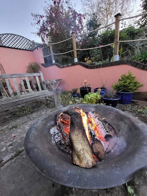 A fire pit with burning wood surrounded by potted plants and a bench. - 2bed-sleeps4-petsok-courtyard & Garden (Totnes)
