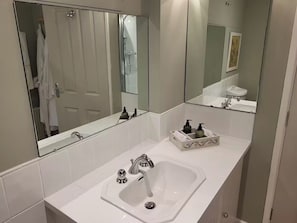 A bathroom with a white sink, a large mirror, and a shower visible in the background. - 2bed-sleeps4-petsok-courtyard & Garden (Totnes)