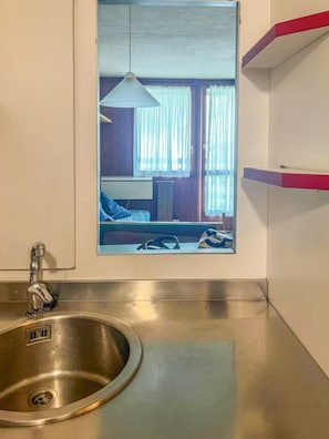 Ein modernes Badezimmer mit einem Edelstahlwaschbecken, einer Pendelleuchte und einem Fenster mit Vorhängen.