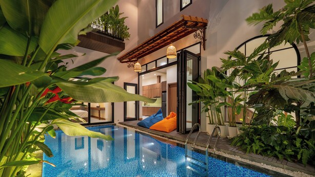 Ein Innenpool mit blau mosaikverlegtem Boden, umgeben von üppiger Bepflanzung und einer Holzpergola mit hängenden Lichtern.