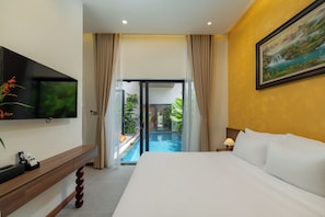 A hotel room with a bed, a TV, a desk, a painting, and a view of an outdoor pool. - Luxury Hoi An Villa – 4BR & Private Pool, Gym, Workplace (Đà N  ẵng)
