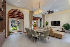 A modern living room with a dining area, a TV, and a ceiling fan. - Luxury Hoi An Villa – 4BR & Private Pool, Gym, Workplace (Đà Nẵng)