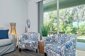 Ein modernes Wohnzimmer mit einer Couch, zwei gemusterten Sesseln, einer Stehlampe und Blick ins Grüne.