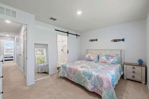 Ein Schlafzimmer mit Bett, Nachttisch, Kommode, einer Tür zu einem anderen Raum und einem Fenster mit Jalousien.