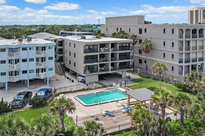 A multi-story hotel with a swimming pool, outdoor seating, and a view of the surrounding area. - Sunrise Beachside Oasis & Pool (Jacksonville Beach)