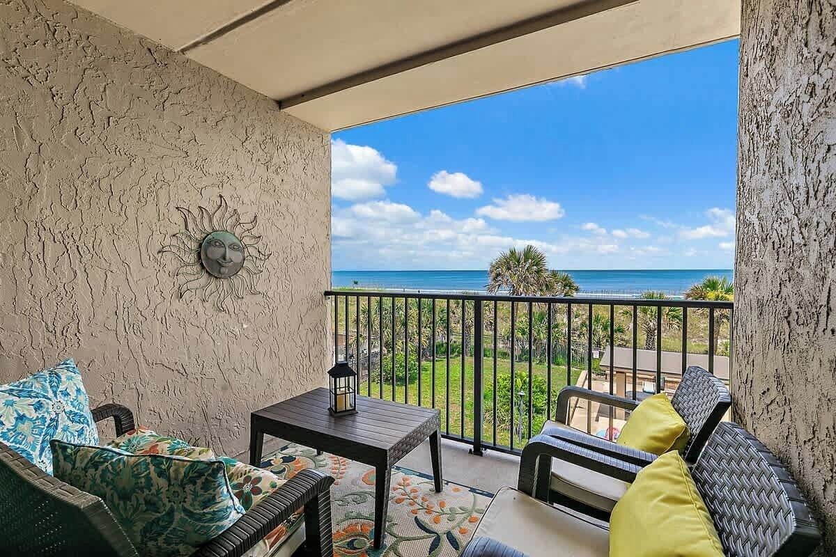 A balcony with a view of the ocean, a table with a lantern, and a sofa with cushions.