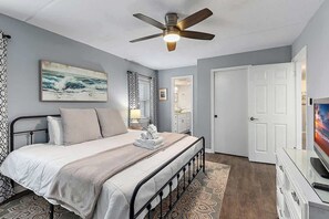 Ein Schlafzimmer mit Bett, Deckenventilator, einem Gemälde, einer Tür und einem Fernseher.