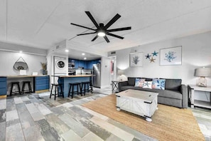 A modern kitchen with a central island, a dining area with a grey sofa, and a ceiling fan. - Ocean Views, Balcony, Private Pool & Beach access, full kitchen with everything you need, Private Laundry in suite. (Jacksonville Beach)