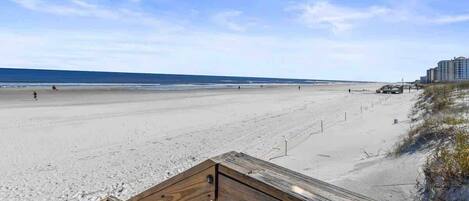 Ein Strand mit einer Holzstege zum Wasser, einem klaren Himmel und einem Gebäude in der Ferne.