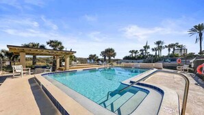 A swimming pool with a pergola, lounge chairs, and palm trees.