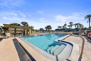 Ein Pool mit Pergola, Liegestühlen und Palmen.