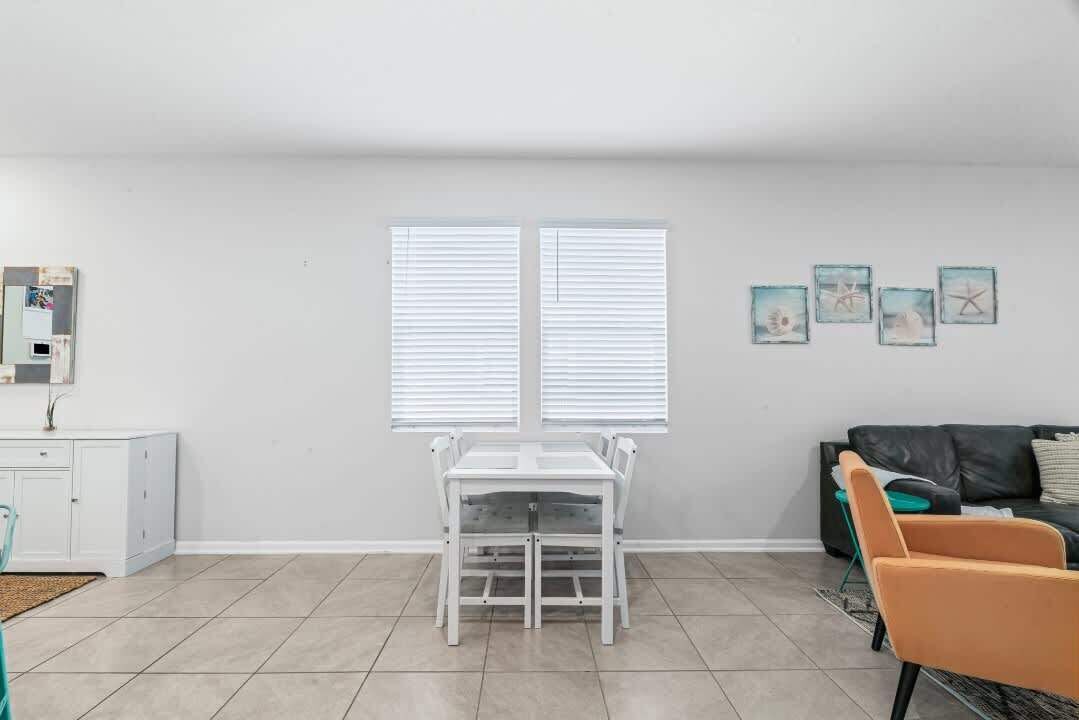 A room with a white table and chairs, a black sofa, and a window with blinds.