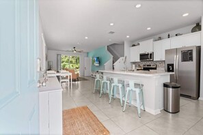 A modern kitchen with white cabinets, a stainless steel refrigerator, and a bar area with stools. - SEA St Augustine - 7 Minutes to Downtown and Beach (St. Augustine)