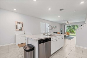 A modern kitchen with white cabinetry, a dishwasher, and a large island with a sink. - SEA St Augustine - 7 Minutes to Downtown and Beach (St. Augustine)