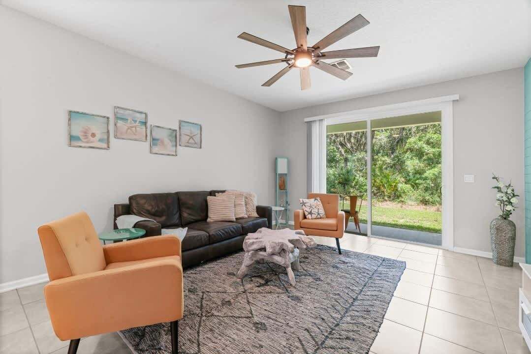 A living room with a ceiling fan, a sofa, two armchairs, a coffee table, and a large window with a view of greenery.