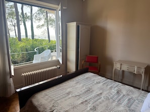 Ein Schlafzimmer mit Bett, Heizkörper, Fenster, Stuhl, Kleiderschrank und einem kleinen Tisch.