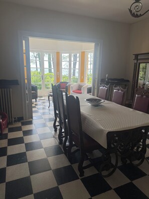 Ein Essbereich mit Schachbrettfußboden, einem Tisch mit gemustertem Tischläufer und Stühlen mit gepolsterten Sitzflächen.