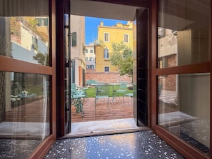 An open door leading to a courtyard with a tiled floor, outdoor furniture, and a view of buildings. - Elegant Waterfront Home with Shared Garden on Venice's Zattere Promenade (Venezia)